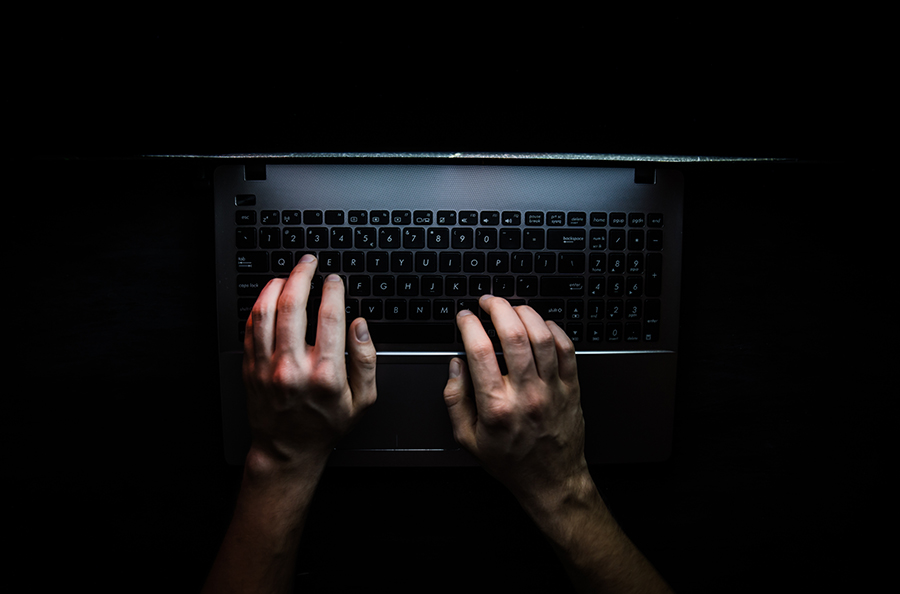 A person's hands typing on a laptop in the dark.