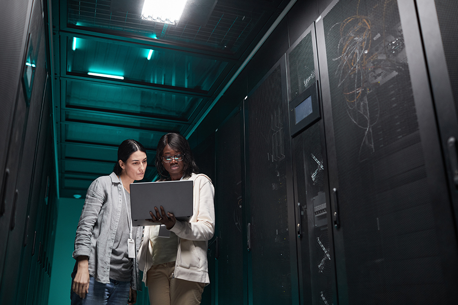 Two women looking at a laptop in a server room.