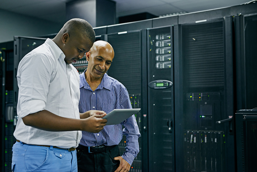 Two men in a server room looking at a tablet.