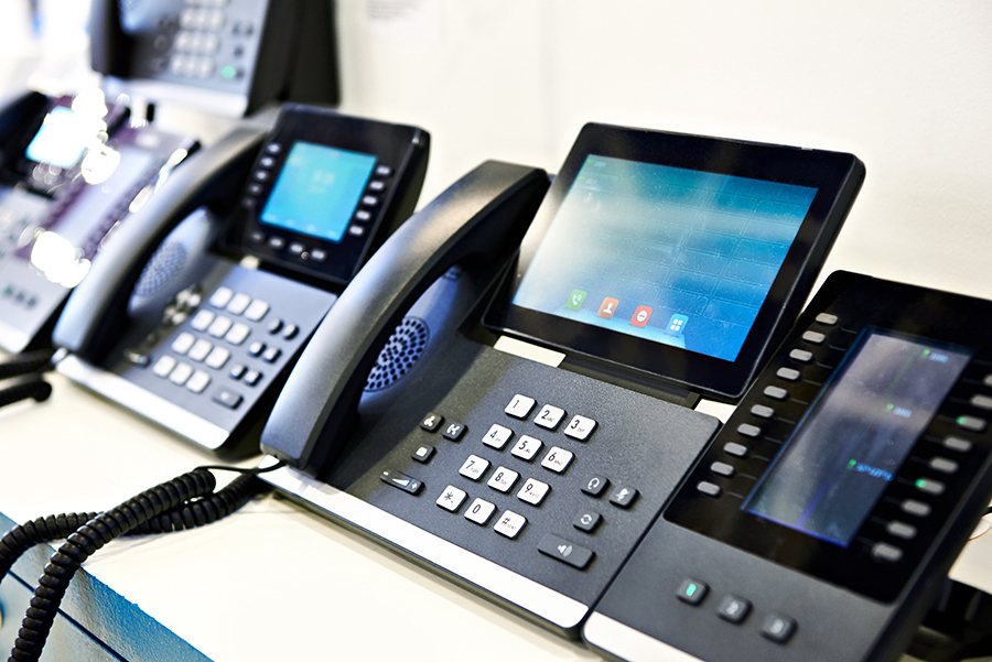 A range of modern voip desk phones displayed on a shelf.